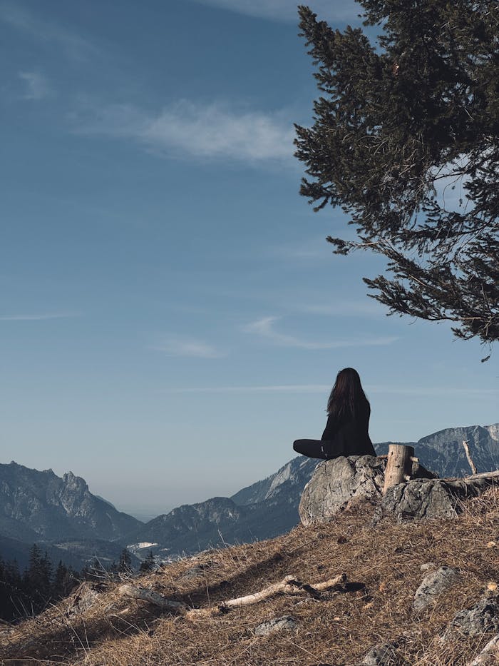 Woman meditating on a mountain overlooking scenic landscapes and forests.